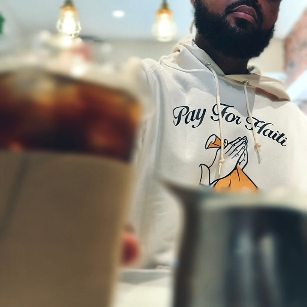 Person wearing a hoodie with 'Pay For Haiti' text and graphic, sitting at a table.