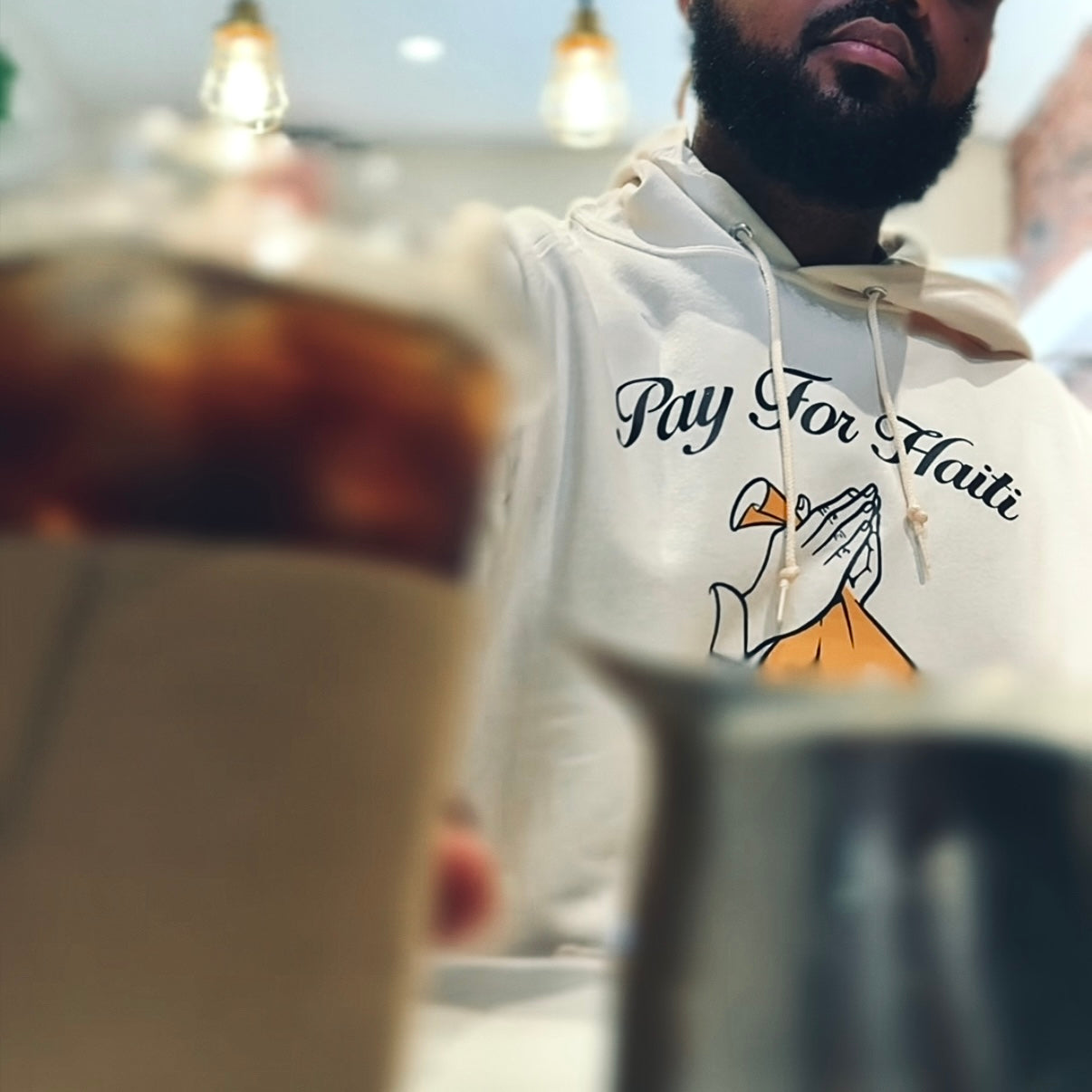 Person wearing a hoodie with 'Pay For Haiti' text and graphic, sitting at a table.