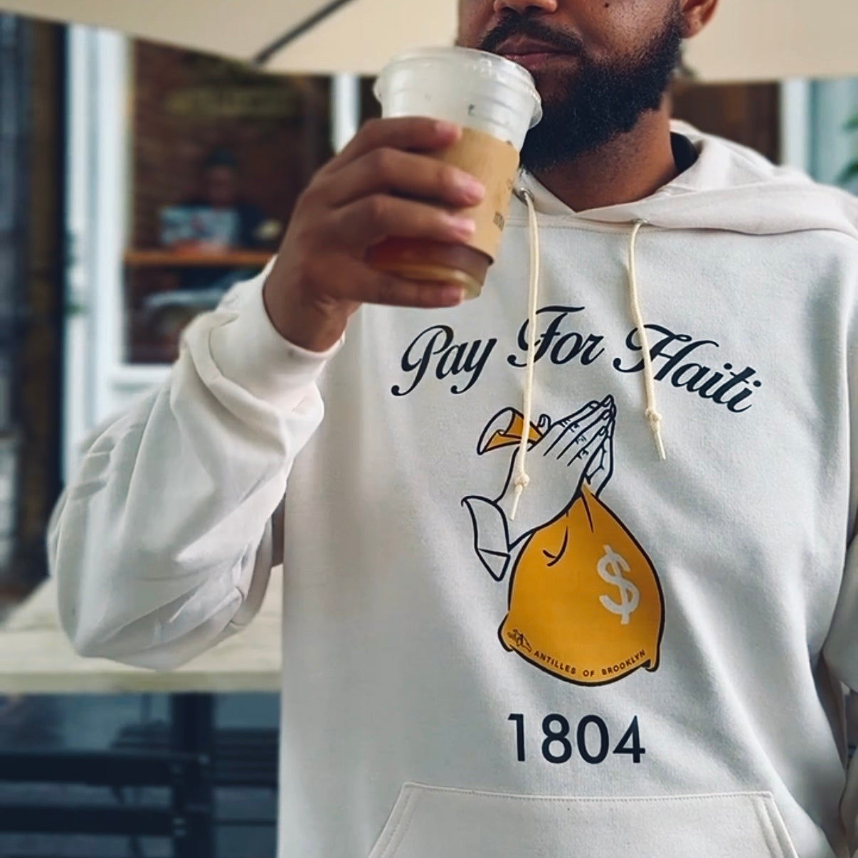 Person wearing a hoodie with a graphic design and text, holding a coffee cup.