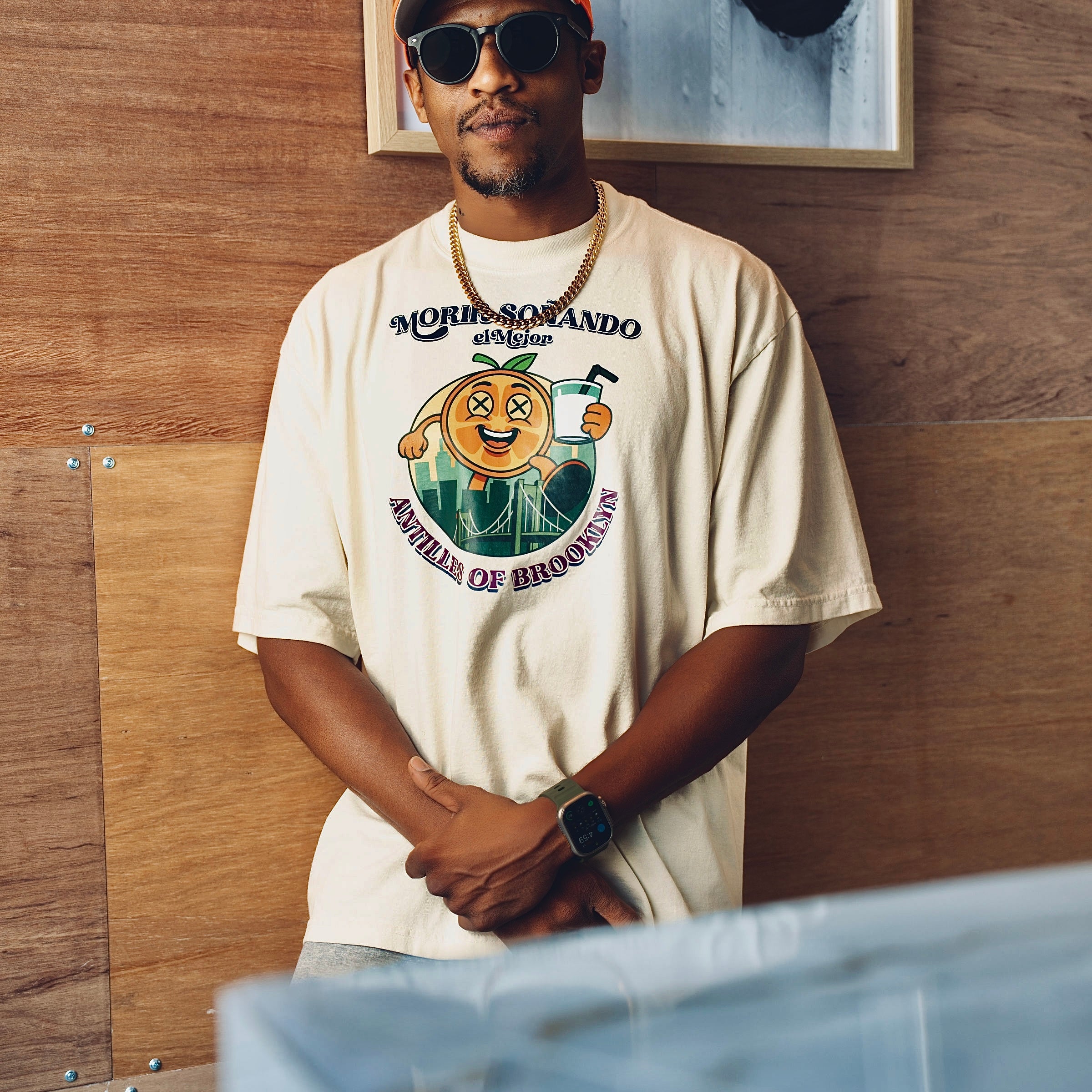 Man wearing a beige t-shirt with a graphic design, standing against a wooden wall.
