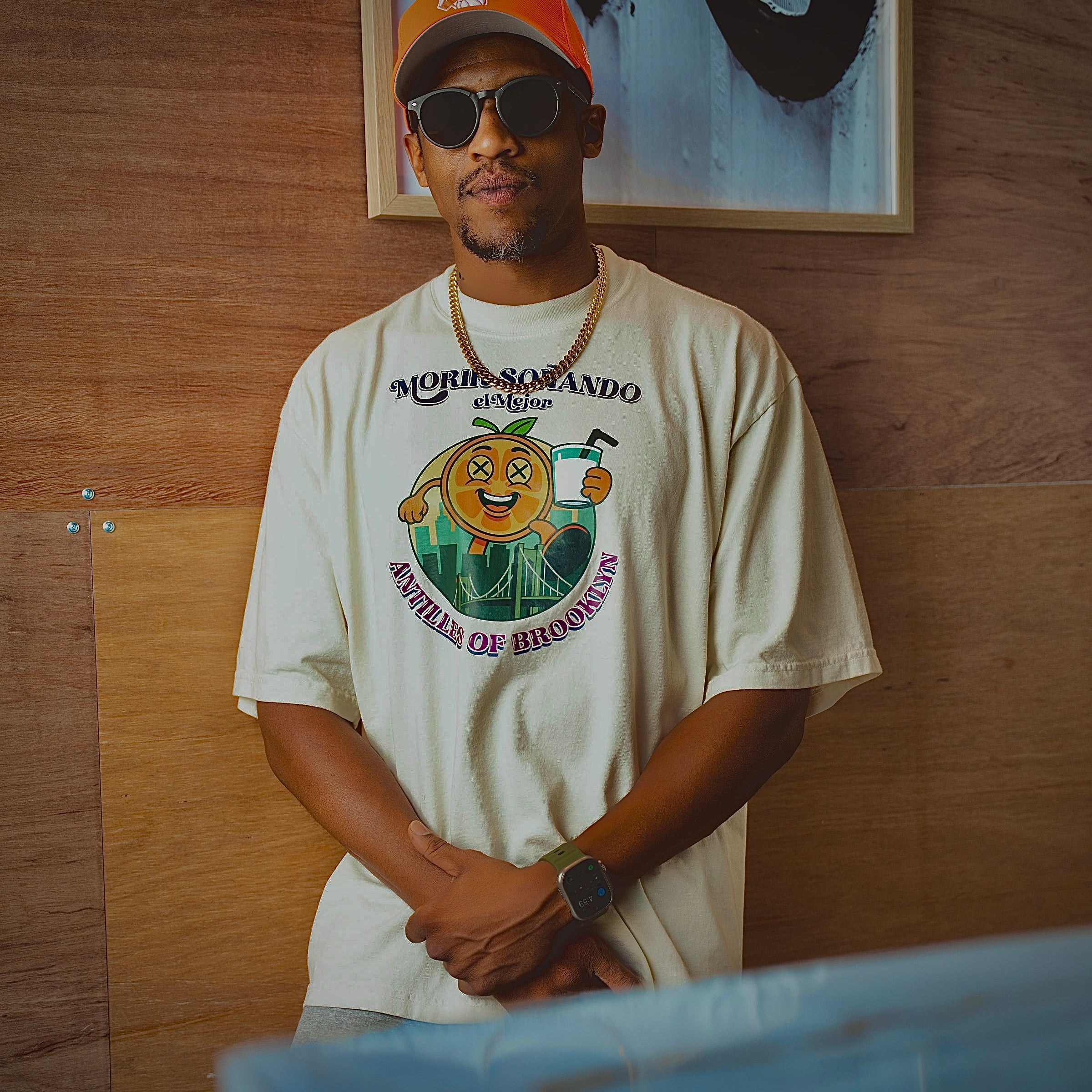 Man wearing a 'Morrisando' t-shirt with a graphic design, standing against a wooden wall.