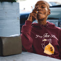 Woman wearing a maroon hoodie with text and graphic, sitting outdoors.