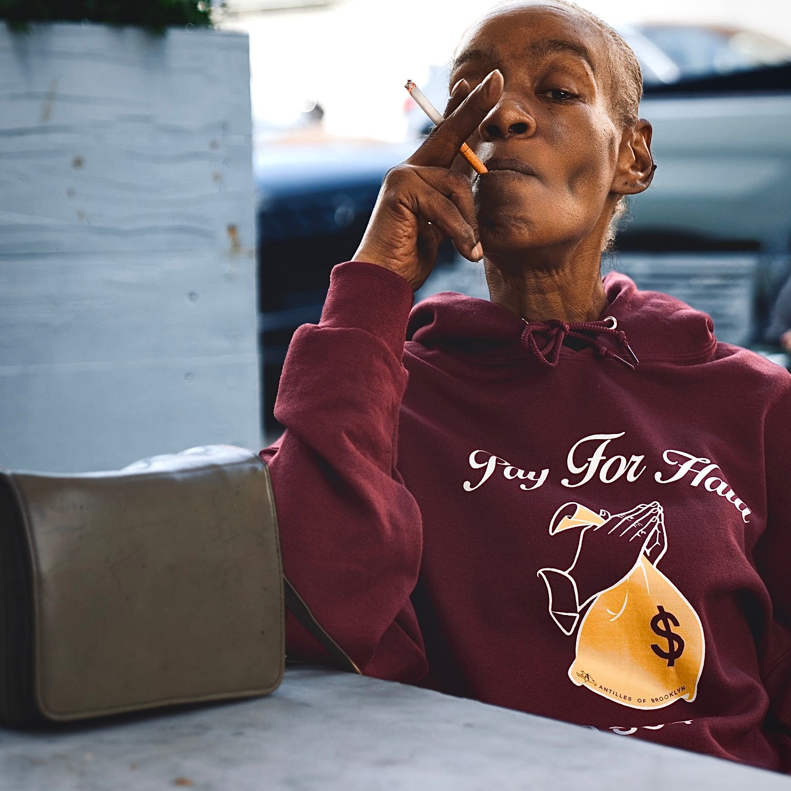 Woman wearing a maroon hoodie with text and graphic, sitting outdoors.