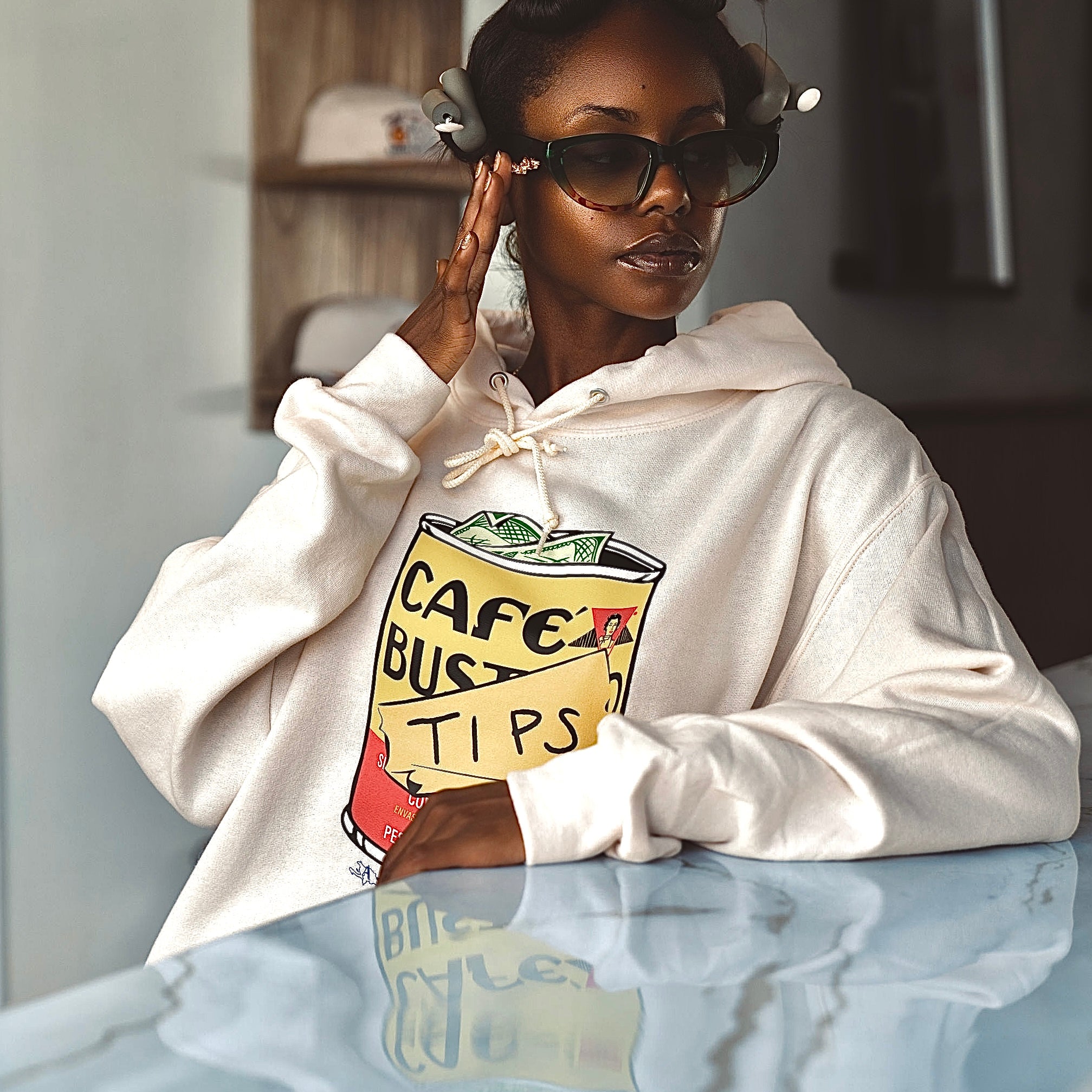 Taylor wearing a cream hoodie with a graphic design of a cafe bustelo and tips text designed by Antilles Cafe.